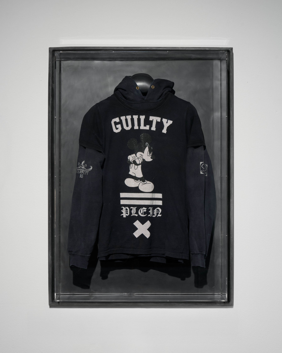 Julian-Jakob Kneer, FANATIC (2), 2025, Archival Misanthropy Records hoodie, Philipp Plein x Disney t-shirt, cast rubber and acrylic glas vitrine, 106 x 76 x 22 cm. Courtesy the artist and Blue Velvet, Zurich. Exhibition views by Andrea Luca Ammann.