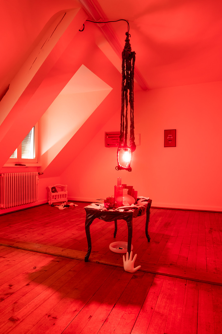 Exhibition View Solo Show Sylvain Gelewski «A Home Is A Home; view on Sylvain Gelewski, AHIAH (low table + lamp), 2024, lacquer, spray on scrap textile and canvas laminated on found antique table, metal, strings, plaster, collected broken porcelain and glass, coloured light, 250 x 50 x 85 cm» at Peripherie 8, Basel, 2024 / Photo: Stefan Schmidlin / Courtesy: Peripherie 8