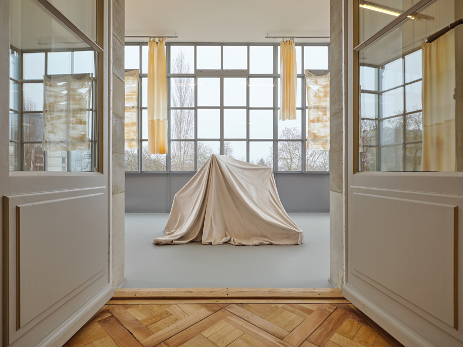 Exhibition View, ‘Stitches: A Haunted House and Other Ghost Stories’ at the Villa Bernasconi, 2026 / Photo by Nicolas Delaroche Studio. From left to right and front to back: Ryan Gander, I is... (i)., 2012, glass fiber, marble powder, Collection Lionel Aeschlimann. Li Tavor, Bright Curtains I, II, III, 2025, pigmented latex curtains, aluminum, carabiners