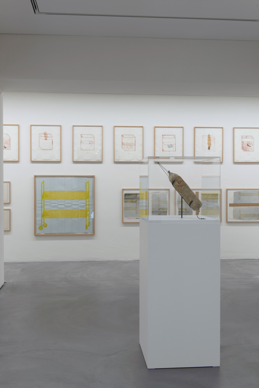 Vorne: Literaturwurst «Die Welt», 1969, (Zerhacktes Exemplar der Zeitung «Die Welt» in zu Wurst geformter Plastikhülle, Streifband), Bündner Kunstmuseum Chur, Wand: Div. Werke aus “Containers-Mappe”, 1972, (div. Drucktechniken), Sammlung Falckenberg
